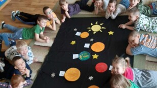 układ słoneczny dzieci leżą na dywanie wokół makiety kosmosu