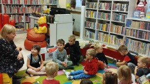 Dzieci siedzą na dywanie w bibliotece i słuchają ksiązki