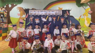 Pasowanie na przedszkolaka dzieci stoją w biretach na tle dekoracji