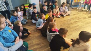 dzieci siedzą na podłodze i oglądają występ