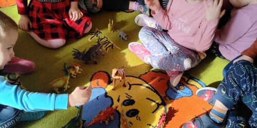 dzieci bawią się figurkami dinozaurów na dywanie