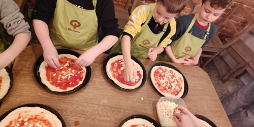 Dzieci posypują serem  placek pizzy