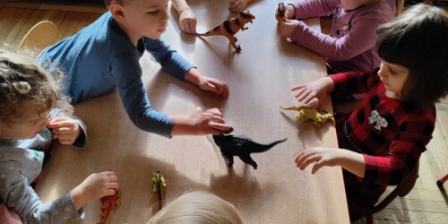 Dzieci bawią się figurkami dinozaurów przy stolikach