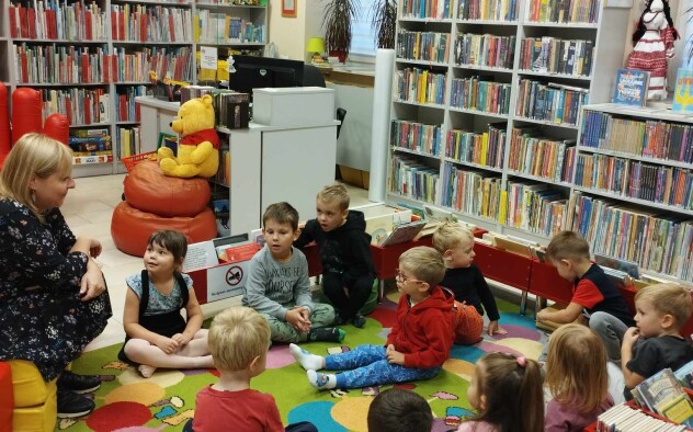Dzieci siedzą na dywanie w bibliotece i słuchają ksiązki