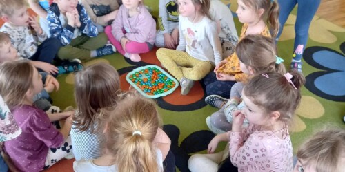 Dzieci siedzą na dywanie z jajkami czekoladowymi na tacce
