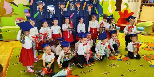 Dzieci w eleganckich strojach stoją na tle dekoracji po pasowaniu